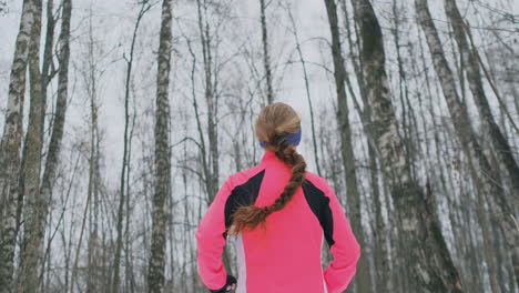 A-young-woman-runs-through-the-park-in-the-winter-in-a-pink-jacket.-View-from-the-back
